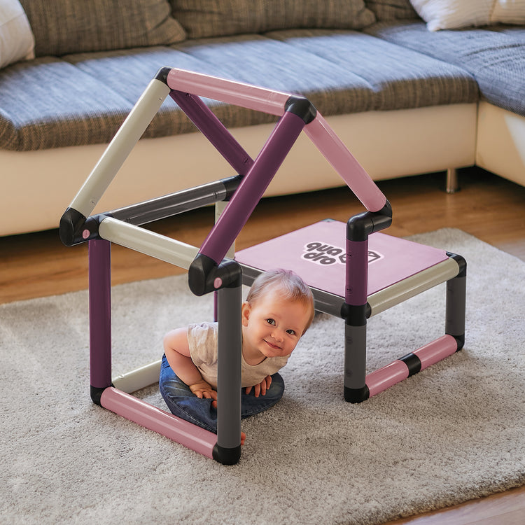 Małe dziecko wygląda spod trójkątnej ramy QUADRO Beginner Berry, platforma po prawej